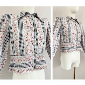 May include: A white, blue and red patterned button-up shirt with a ruffled hem. The shirt has a gingham pattern and a floral print.