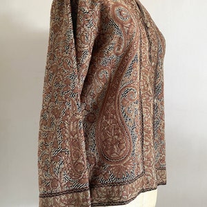 May include: A brown embroidered jacket with a paisley pattern. The jacket has a mandarin collar and long sleeves.