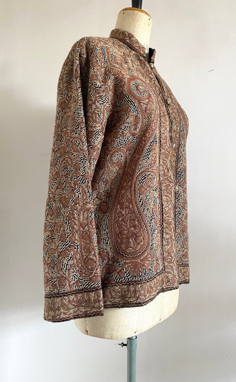 May include: A brown embroidered jacket with a paisley pattern. The jacket has a mandarin collar and long sleeves.