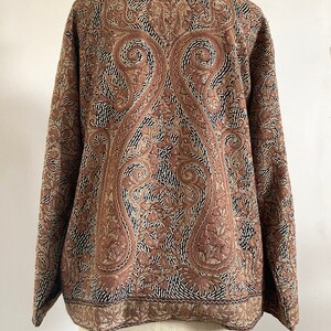 May include: A brown jacket with a paisley pattern embroidered on the back. The jacket has a stand-up collar and long sleeves.