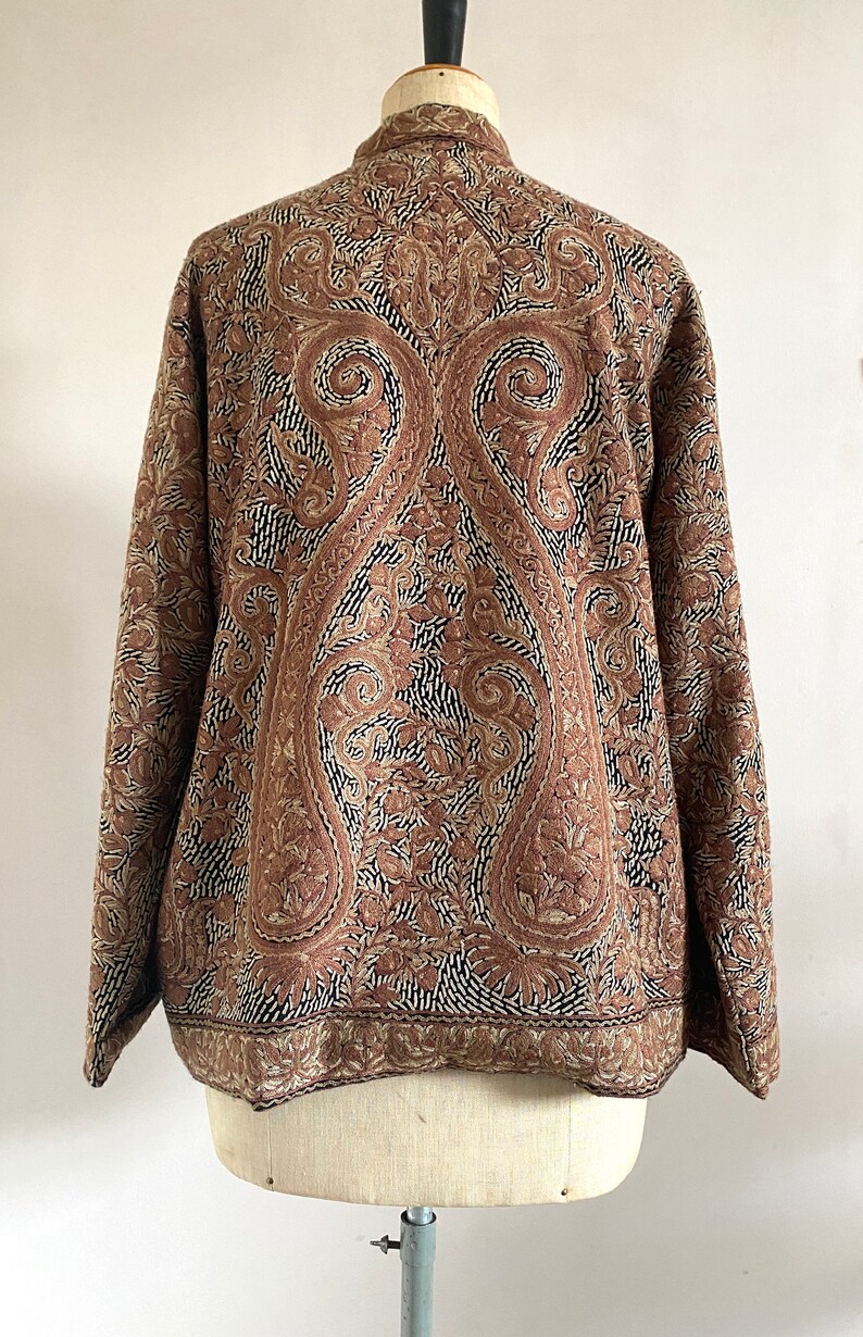 May include: A brown jacket with a paisley pattern embroidered on the back. The jacket has a stand-up collar and long sleeves.