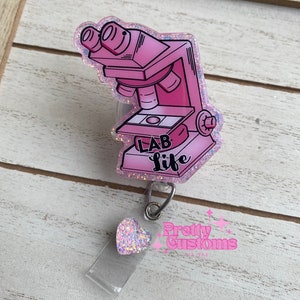May include: Pink glitter microscope badge holder with the text "Lab Life" and a pink glitter heart charm. The badge holder is attached to a clear plastic strap with a silver clip.