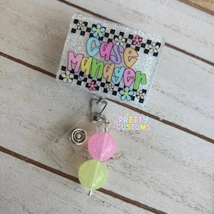 May include: A badge reel with the words "Case Manager" in colorful bubble letters. The badge reel has a glittery background with a black and white checkered pattern and flower accents. Two pastel-colored, glittery beads dangle from the reel.