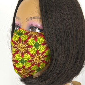 May include: A face mask with a green, red, and yellow floral pattern. The mask is made of fabric and has a pleated design.