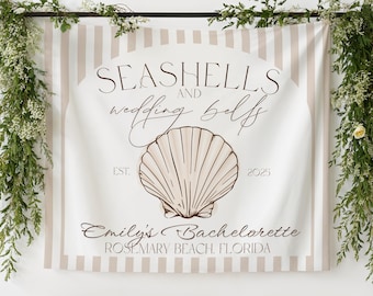 Op de afbeelding: Een rechthoekige stoffen achtergrond met verticale beige en witte strepen. Het midden toont een witte boog met een grote bruine schelpillustratie, de tekst SEASHELLS AND wedding bells, EST. 2025, Emily's Bachelorette en ROSEMARY BEACH, FLORIDA.