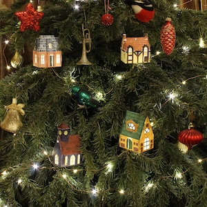 May include: A Christmas tree decorated with miniature houses, a star, a bird, a bell, and a trumpet. The tree is also decorated with a string of white lights.