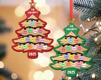 Op de afbeelding: Twee houten kerstboomversieringen in de vorm van een boom, één rood en één groen. Ze tonen de tekst "THE WILLIAM'S" en "2025", met namen en kleurrijke lichtjes. Elk heeft een rood lint om op te hangen.