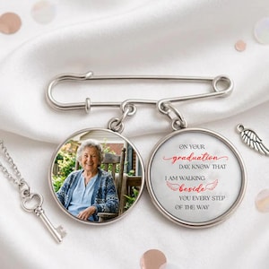May include: A silver-toned graduation pin with two circular pendants. One pendant features a photo of a smiling woman, the other has text that reads "On Your Graduation Day, Know That I Am Walking Beside You Every Step of the Way."