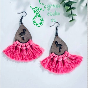 May include: Pink tassel earrings with a wooden flamingo cutout. The earrings are handmade and feature a pink tassel design. The earrings are made by Green Snake Co.