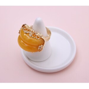 K&ouml;nnte beinhalten: Ein goldener Ring mit einem gelben Jade-Stein, der in einem filigranen Design eingefasst ist.