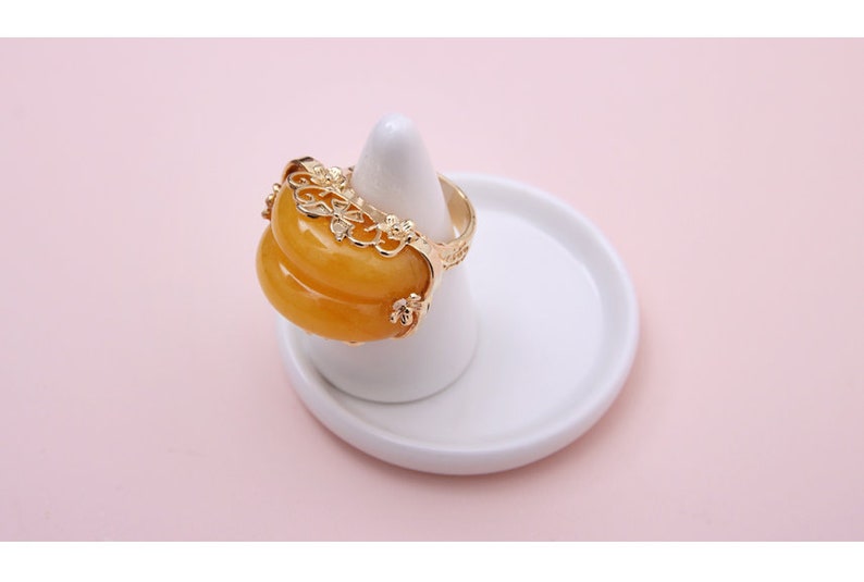 K&ouml;nnte beinhalten: Ein goldener Ring mit einem gelben Jade-Stein, der in einem filigranen Design eingefasst ist.