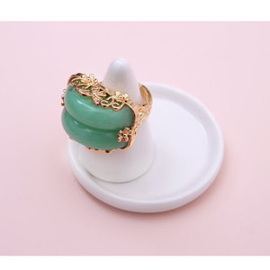 K&ouml;nnte beinhalten: Ein goldener Ring mit einem gr&uuml;nen Jade-Stein, der in einem filigranen Blumenmuster gefasst ist.