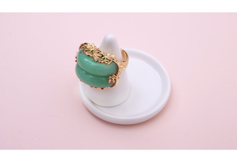 K&ouml;nnte beinhalten: Ein goldener Ring mit einem gr&uuml;nen Jade-Stein, der in einem filigranen Blumenmuster gefasst ist.