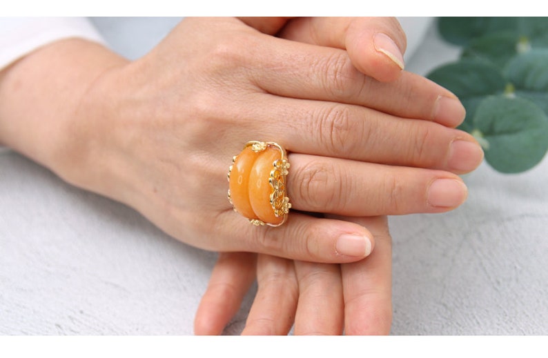K&ouml;nnte beinhalten: Ein goldener Ring mit einem gro&szlig;en, ovalen, orangefarbenen Edelstein. Der Ring ist mit aufwendigen goldenen Details um den Stein herum verziert.