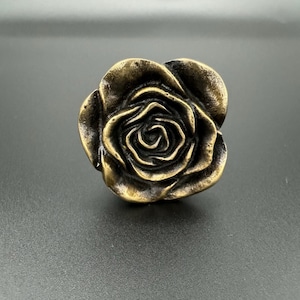 Pode incluir: Um bot&atilde;o de arm&aacute;rio de metal dourado em forma de rosa.