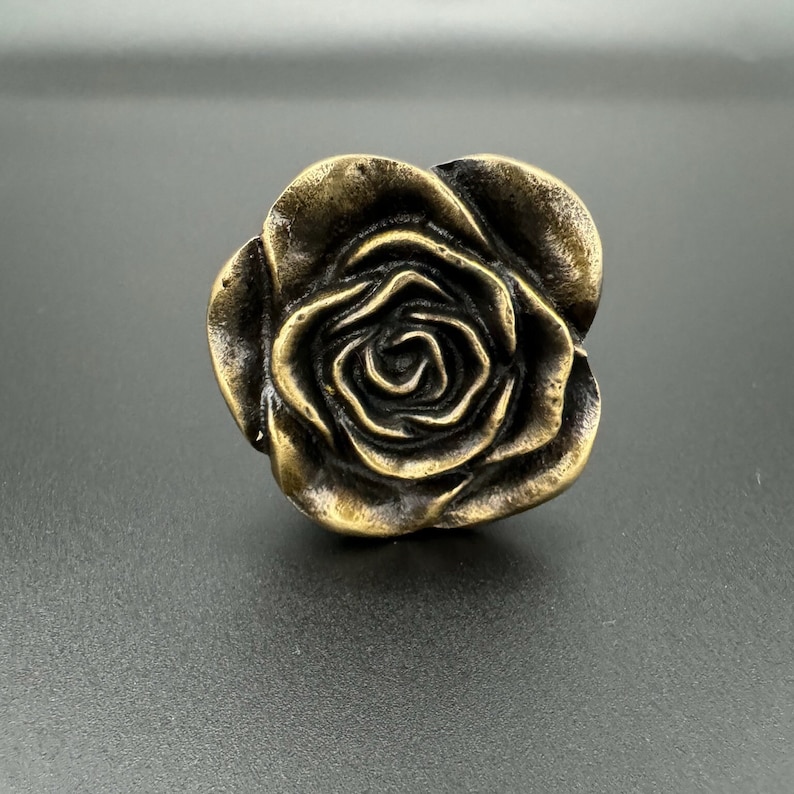 Pode incluir: Um bot&atilde;o de arm&aacute;rio de metal dourado em forma de rosa.