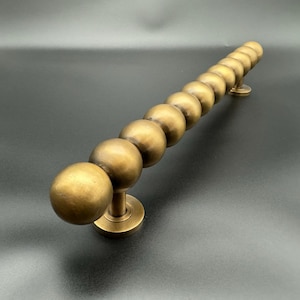 May include: A long, brass door handle with a beaded design. The handle is made of a series of round, smooth knobs that are connected together.