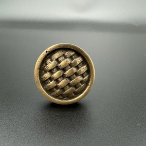 Pode incluir: Um bot&atilde;o de arm&aacute;rio redondo de lat&atilde;o com um padr&atilde;o tecido.