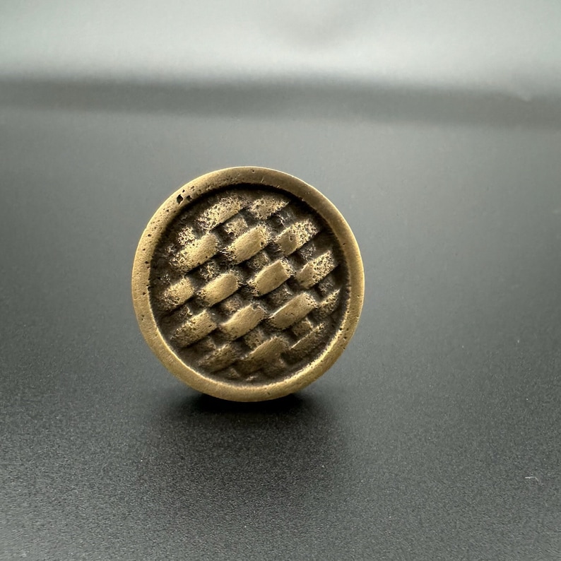 Pode incluir: Um bot&atilde;o de arm&aacute;rio redondo de lat&atilde;o com um padr&atilde;o tecido.