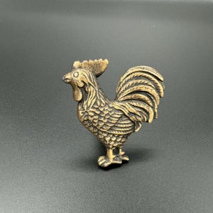 Pode incluir: Uma figura de galo de metal dourado com penas detalhadas e uma superf&iacute;cie texturizada.