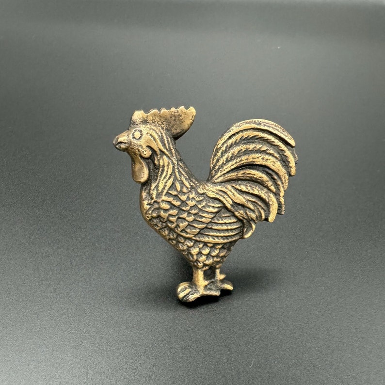 Pode incluir: Uma figura de galo de metal dourado com penas detalhadas e uma superf&iacute;cie texturizada.