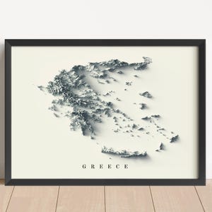Op de afbeelding: Ingelijste grijstinten reliëfkaart van Griekenland, met gedetailleerde topografische kenmerken. De kaart staat tegen een crèmekleurige achtergrond, met het woord "GREECE" onderaan. De lijst is zwart.