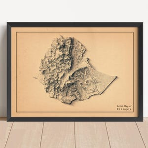 May include: A framed relief map of Ethiopia, depicting the country's terrain in beige and brown tones. The map is set against a tan backdrop and framed in black. The text "Relief Map of Ethiopia" is displayed at the bottom right.