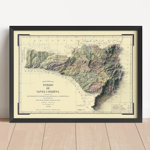 May include: Framed vintage map of Santa Catarina, Brazil, in a black frame. The map features detailed topography with shades of green, brown, and beige. Text in Portuguese is visible, including the title "Estado de Santa Catarina."