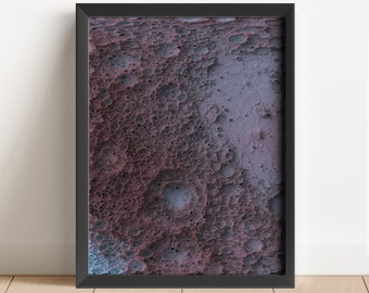 May include: A framed abstract print with a textured, cratered surface in shades of purple, blue, and gray.