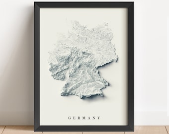 May include: A black framed print of a topographic map of Germany. The map is in shades of grey and white, with the country's borders clearly defined. The word "GERMANY" is printed in black at the bottom of the print.