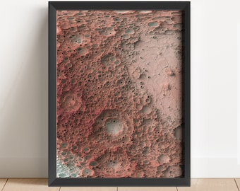 May include: A framed abstract print of a textured, cratered surface in shades of pink, red, and grey. The surface resembles a moon or other celestial body.