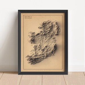 May include: A framed relief map of Ireland featuring a tan background with dark brown topographical shading. The map displays the island's terrain with high contrast shadows and includes the text Relief Map of Ireland in the upper left corner.