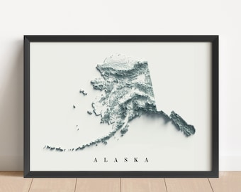 May include: A black framed print of a 3D topographic map of Alaska. The map is in shades of gray and white, with the state's name printed in black at the bottom.