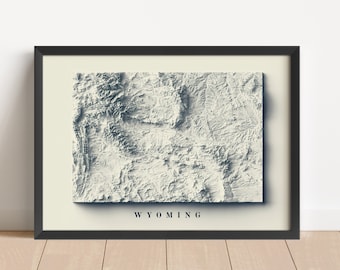 May include: A black framed print of a topographic map of Wyoming. The map is in shades of gray and white, with the state name "WYOMING" printed in black at the bottom.