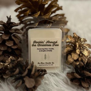 May include: A clear plastic container holding a rectangular wax melt, with the text "Rockin' Around the Christmas Tree" on the label. The label also reads "Featuring Pine, Vanilla, & Boughs of Holly." The wax melt is surrounded by several pine cones.