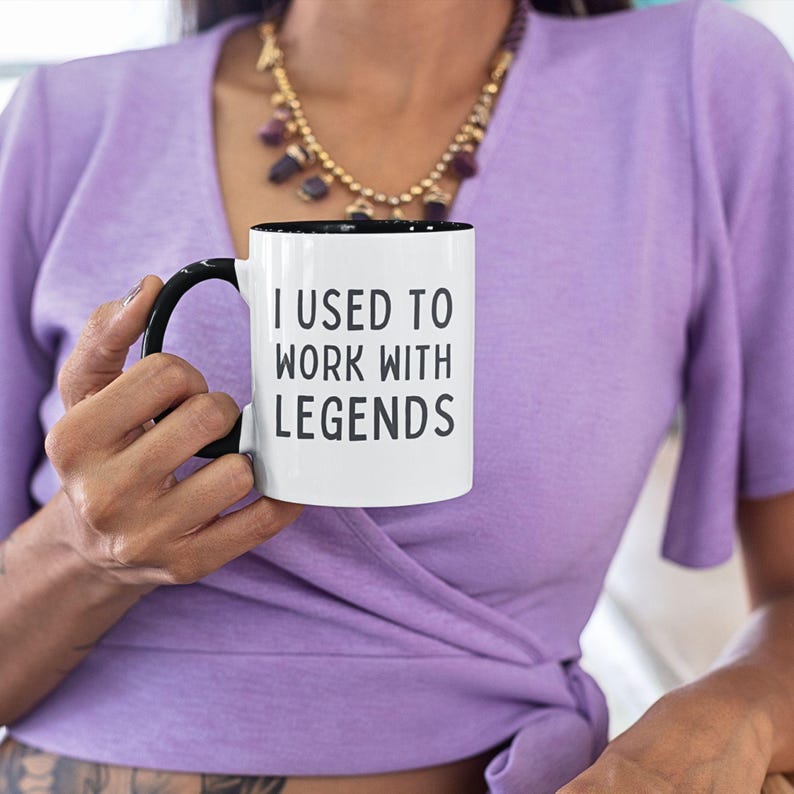 May include: White coffee mug with a black rim and handle. The mug has the text "I used to work with legends" printed in black.