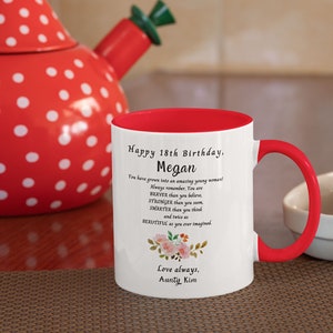 May include: White ceramic mug with a red rim and handle. The mug has a floral design and text that reads "Happy 18th Birthday, Megan. You have grown into an amazing young woman! Always remember, You are BRAVER than you believe, STRONGER than you seem, SMARTER than you think and twice as BEAUTIFUL as you ever imagined. Love always, Aunty Kim."