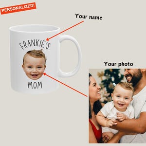 以下が含まれることがあります： 白いセラミックマグカップ、赤ちゃんのお顔と「FRANKIE'S MOM」の文字入り。左上の小さな赤いバナーには「PERSONALIZED！」と書かれています。右側には家族写真があります。