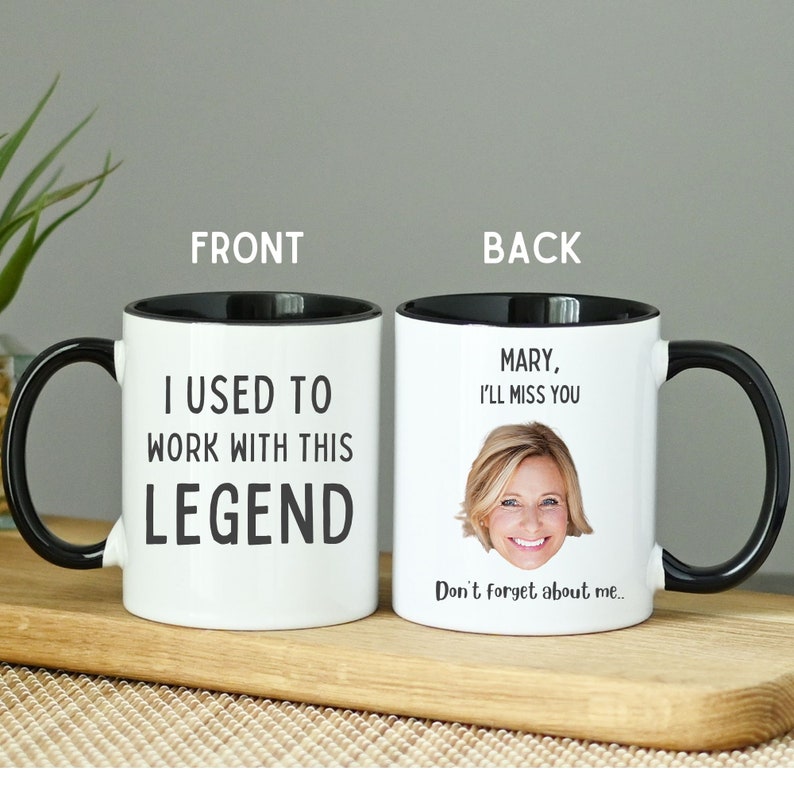 Op de afbeelding: Een witte keramische mok met een zwarte rand en handvat. De voorkant van de mok heeft de tekst "Ik heb met deze legende gewerkt". De achterkant van de mok heeft een foto van een vrouw en de tekst "Mary, ik zal je missen. Vergeet me niet..."