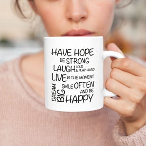May include: White ceramic mug with black text that reads "Have Hope, Be Strong, Laugh Loud & Play Hard, Live in the Moment, Smile Often, and Be Happy".