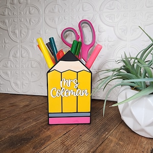 May include: Yellow pencil-shaped desk organizer with a pink eraser and a black pencil lead. The organizer has the name "Mrs. Coleman" written on the front.