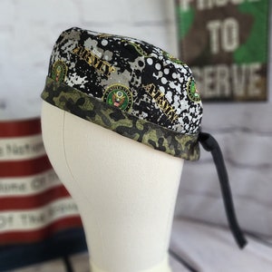 May include: A black and green camouflage patterned surgical cap with the word "ARMY" printed on it. The cap has a black tie and features the United States Army seal.