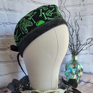 May include: Black scrub hat with a green skeleton print. The hat has a tie on the back.