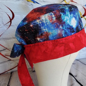 May include: A red and blue galaxy print scrub hat with a red tie. The hat has a red trim and is made of soft, comfortable fabric.
