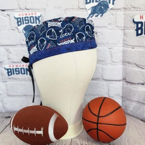 May include: A navy blue scrub cap with a pattern of white bison and the words "HOWARD BISON". The cap has a blue trim and black ties. A brown football and orange basketball are in the foreground.