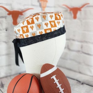 May include: A patterned scrub cap featuring a checkerboard design in orange, gray, and white. The cap has a black band and ties. A basketball and a football are in the foreground.