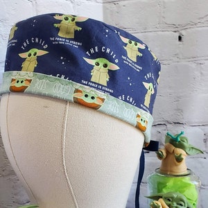 May include: A blue and green patterned scrub hat with the text "The Child" and "The Force is Strong with this little one".