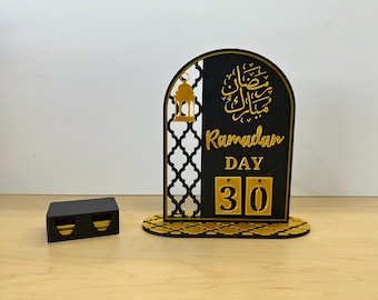 May include: Black wooden Ramadan countdown calendar with gold Arabic calligraphy, a gold lantern design, and a gold and black patterned base. The calendar features a flip-style design with the number 30 displayed.
