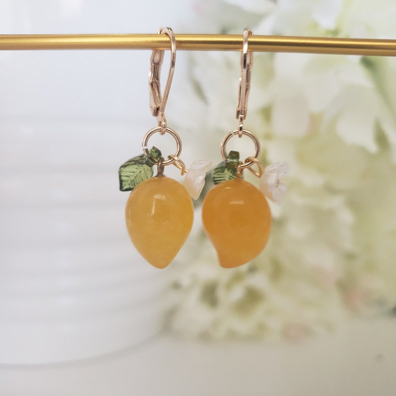 May include: A pair of gold earrings with a yellow lemon charm, green leaves, and white flower accents.