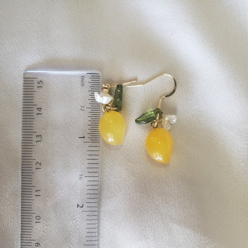 May include: A pair of gold lemon earrings with green leaves and white flower accents. The earrings are approximately 1 inch long.